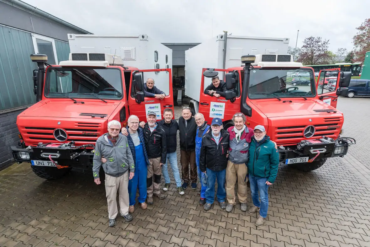 Madagaskar-Mobile-Klinik – Gruppe von Männern steht vor zwei Unimogs, auf deren Ladefläche Container montiert sind