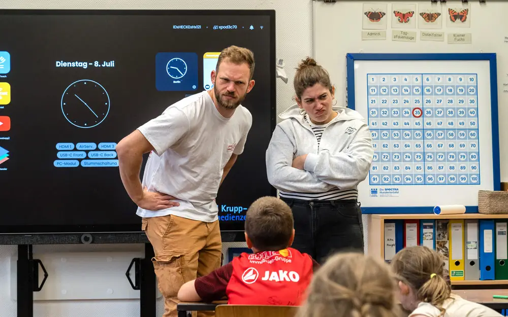 Streitkultur in der Grundschule – Konflikte erkennen und lösen Zwei Theaterpädagogen spielen eine Konfliktszene im Klassenraum vor Grundschulkindern