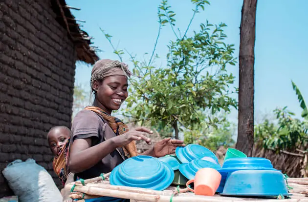 Malawi – Frau mit auf dem Rücken gebundenen Kind kümmert sich im Freien um Abwasch