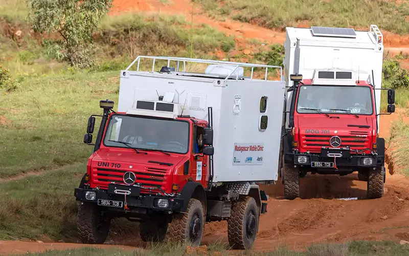 DEICHMANN-Stiftung | Madagascar Mobile Clinic – Gesundheitsangebote erreichbar machen – geländegängige Fahrzeuge – Unimog  Alt-Tag<br />
Madagascar Mobile Clinic – zwei geländegängige Fahrzeuge vom Typ Unimog fahren über eine schlammige, buckelige Lehmpiste<br />
