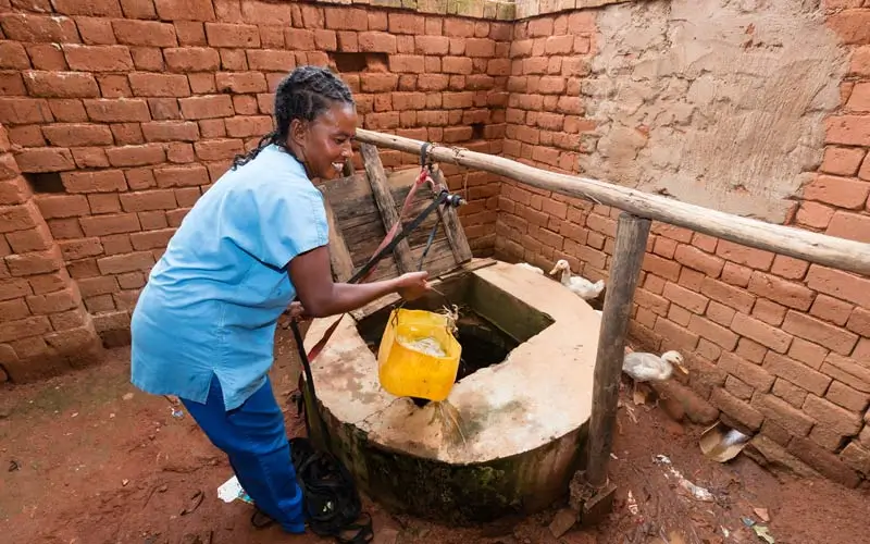 DEICHMANN-Stiftung | Madagascar Mobile Clinic – Gesundheitsangebote an schwer erreichbaren Orten – Frau am Brunnen – Sauberes Wasser schützt vor Infektionen Madagascar Mobile Clinic – Frau in Madagaskar zapft Wasser aus einem mit Deckel verschließbaren Brunnen – sauberes Wasser verhindert Krankheiten