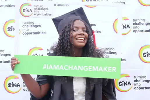 Deichmann Stiftung | Sozialunternehmen Uganda – SINA-Alumni Deichmann Stiftung fördert Sozialunternehmen Uganda – SINA-Alumni – strahlendes Mädchen – hält stolz Changemaker-Schild hoch