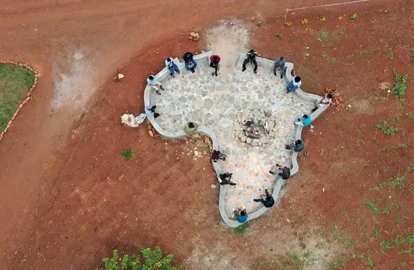 Deichmann Stiftung | Sozialunternehmen Uganda – Kapitalgeber für afrikanische Unternehmen Sozialunternehmen Uganda – mehrere Personen sitzen an einer Feuerstelle, die in Form des afrikanischen Kontinents angelegt ist – globale Investoren für Uganda