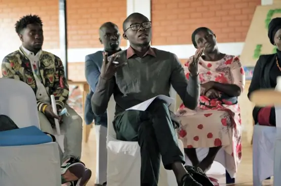 Deichmann Stiftung | Sozialunternehmen Uganda – unternehmerische Kompetenzen Sozialunternehmen Uganda – Personen beim Training – Person im Bildvordergrund stellt eine Frage – unternehmerische Kompetenzen erwerben